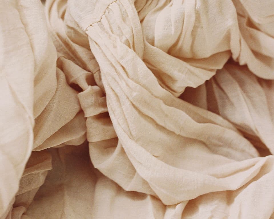 Draped lyocell material in a natural cream tone, highlighting the fluid texture and softness characteristic of TENCEL™ Lyocell fibers